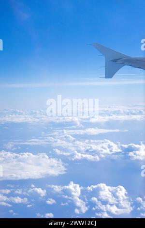 Flügel eines Flugzeugs, der über flauschigen Wolken schwingt, vom Fenstersitz erfasst. Aus der Vogelperspektive zeigt die heitere Schönheit des Himmels. Stockfoto