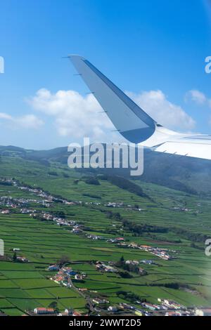 Flügel eines Flugzeugs, der über Felder auf Terceira Island auf den Azoren schwingt. Luftaufnahme vom Fenstersitz aus. Stockfoto