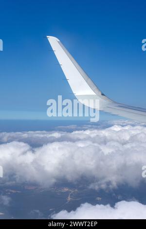 Flügel eines Flugzeugs, der über flauschigen Wolken schwingt, vom Fenstersitz erfasst. Aus der Vogelperspektive zeigt die heitere Schönheit des Himmels. Stockfoto