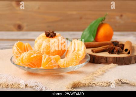 Teller mit frischen Mandarinensegmenten und Gewürzen auf hölzernem Hintergrund Stockfoto