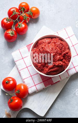 Traditionelle türkische Tomatenpaste in Schüssel mit frischen Tomaten auf rustikalem Tisch, hausgemachte gesunde Speisen Stockfoto