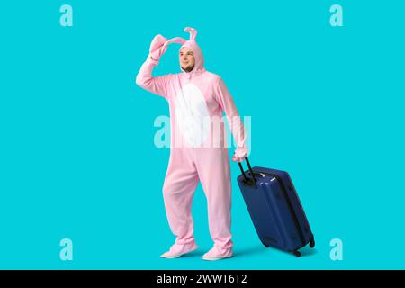 Junger Mann im Hasenkostüm mit Koffer auf blauem Hintergrund. Osterfeier Stockfoto