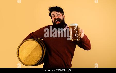 Bierzeit. Glückliche Brauerei mit Holzfass und Becher Bier. Bärtiger Mann, der gebrautes Bier in einem Pub oder einer Bar verkostet. Oktoberfest. Deutsche Traditionen Stockfoto