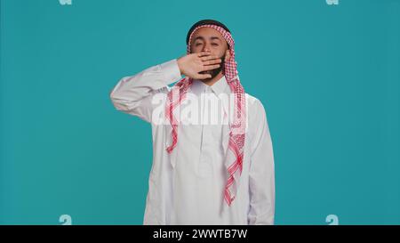 Schlafender Kerl, der im Studio gähnt, sich extrem schläfrig anfühlt und fast vor der Kamera eingeschlafen ist. Islamische Person mit du und Kufiyah, die erschöpft sind, unter Müdigkeit leiden. Stockfoto