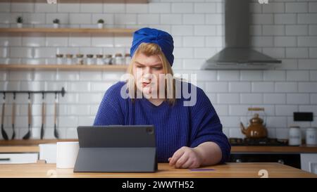 Erwachsene übergewichtige Frau geben Sie die Kreditkartennummer auf dem Tablet-Computer ein, um online einzukaufen, macht sichere, einfache elektronische Zahlung im Fernverkehr, während Sie drinnen sitzen Stockfoto