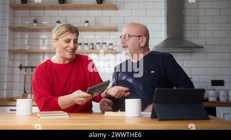 Pensioniertes Paar sitzt in der Küche und macht Papierkram, überprüft Rechnungen, Bankkreditzahlungen, diskutiert unbezahlte Steuern. Das Familiengeld der alten Großeltern Stockfoto