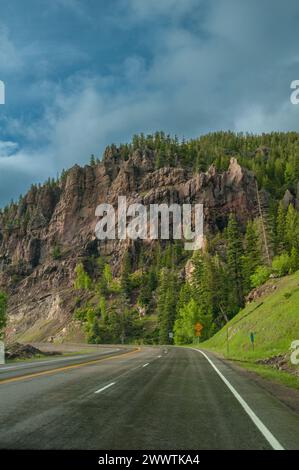 Dieses lebendige Bild fängt eine malerische Reise auf einer Straße ein, die durch zerklüftete Berge unter einem hellblauen Himmel führt Stockfoto