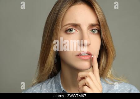 Frau mit Herpes, die Creme auf die Lippe aufträgt, vor hellgrauem Hintergrund Stockfoto