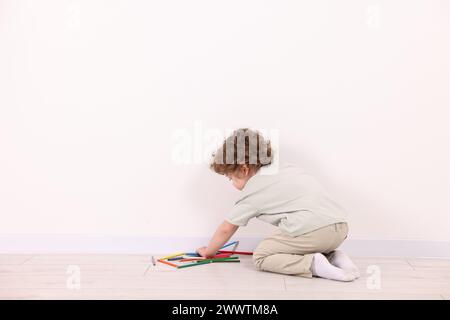 Kleiner Junge mit bunten Bleistiften an der weißen Wand drinnen. Leerzeichen für Text Stockfoto