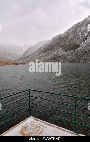 Eine hölzerne Plattform mit Metallgeländern auf der Oberfläche eines wunderschönen Sees, umgeben von schneebedeckten Bergen an einem bewölkten Herbsttag. Kok-Kol-See, Alt Stockfoto