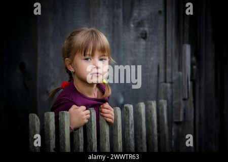 Ein süßes kleines Mädchen schaut hinter einem rustikalen Holzzaun raus. Stockfoto