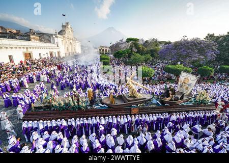 Antigua, Guatemala. März 2024. Katholische Pönitenten tragen den massiven Prozessionswagen, während er sich während der 20-stündigen Palmensonntag-La Reseña-Prozession am 24. März 2024 in Antigua, Guatemala, um den zentralen Platz mit dem Vulkan Agua und der Kathedrale von St. James San José bewegt. Die opulenten Prozessionen, detailgetreuen Alfombras und jahrhundertealten Traditionen ziehen mehr als 1 Million Menschen in die alte Hauptstadt. Quelle: Richard Ellis/Richard Ellis/Alamy Live News Stockfoto