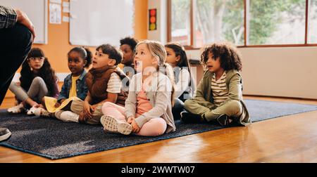 Kleine Kinder, die den Vokal sagen, hören sich laut an. Gruppe von Grundschulkindern, die im Unterricht sitzen. Grundschüler, die an einer mündlichen Teilnahme teilnehmen Stockfoto