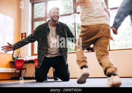 In einer Grundschule laufen die Schüler ihrem Lehrer in die Arme. Ein Lehrer begrüßt seine Schüler mit offenen Armen in einer Grundschule. Kinder begeistern Stockfoto