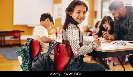 Genießen Sie einen Kunst- und Kreativkurs. Ein junges Mädchen lächelt in die Kamera, während es in einem Klassenzimmer sitzt. Kindererziehung an einer Grundschule. Stockfoto