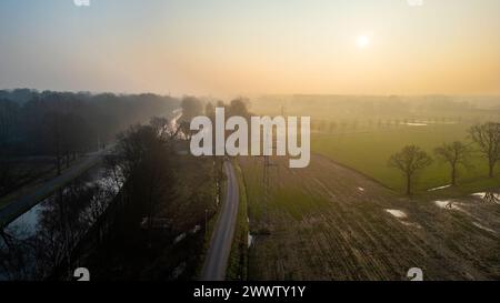 Die Morgensonne strahlt ein goldenes Leuchten auf einer sich schlängelnden Straße und einem Kanal und schneidet durch die nebelbelbeladene Landschaft. Sonnenaufgang über gewundenen Straßen und Kanal in nebeliger Landschaft. Hochwertige Fotos Stockfoto