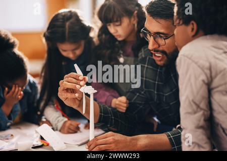 Kinder lernen erneuerbare Energien mit einem 3D-Windmühlenmodell im Wissenschaftsunterricht kennen. Männlicher Grundschullehrer gibt eine praktische Lektion über Wind p Stockfoto