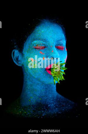 Neon, Farbe und Gesicht der Frau im Atelier mit Pflanze für organische Kunst, Pflanzenästhetik oder Kosmetik. Glow Make-up, Person oder fluoreszierende Glitzer für uv Stockfoto