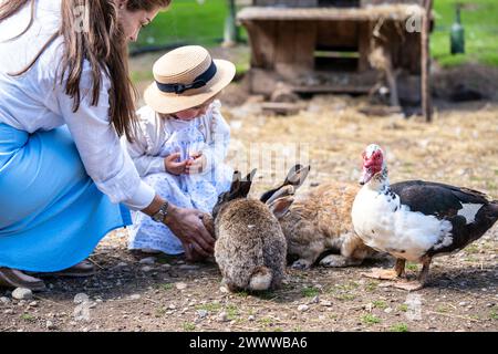 Mutter und kleine Tochter füttern Kaninchen und Vögel auf der Farm Stockfoto