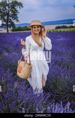 Eine schöne Frau mit Hut und Tasche geht durch ein Lavendelfeld Stockfoto