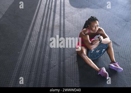 Eine starke afroamerikanische Frau sitzt auf einer schwarzen Matte im Fitnessstudio mit Kopierraum Stockfoto