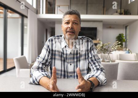 Ein birassischer Mann mittleren Alters sitzt zu Hause an einem Tisch in einem Video Stockfoto