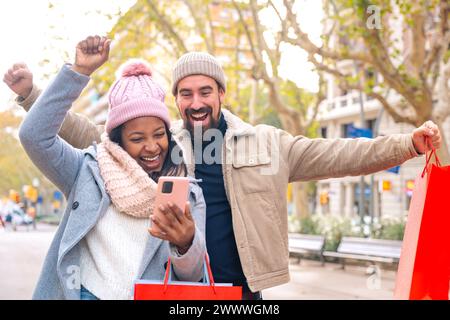 Glückliches multirassisches junges Paar gewinnt mit einer Online-Wetten-App. Im Freien Stockfoto
