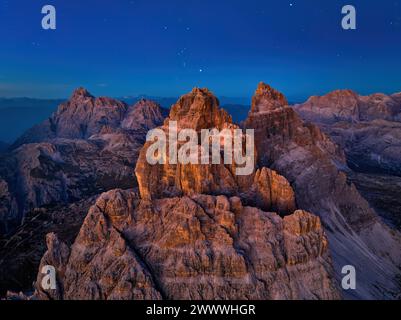 Aus der Höhe der drei Zinnen di Lavaredo Gipfel aus der Vogelperspektive orange beleuchtet vom blauen adrk-Himmel, erster Stern. Bergpanorama der Dolomiten. Stockfoto