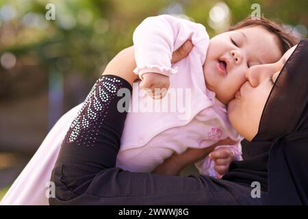 Muslimische Mutter, draußen und küssen Baby für Pflege, Verbindung und Verbundenheit im Sommer. Mama, Kind und Liebe auf der Wange für das Kind, entzückendes Kind und Stockfoto