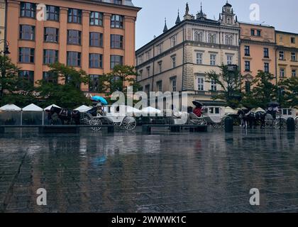 Pferdekutschen auf dem Marktplatz an einem herbstlichen Regentag. Krakau, Polen. Redaktionelles Foto. Stockfoto