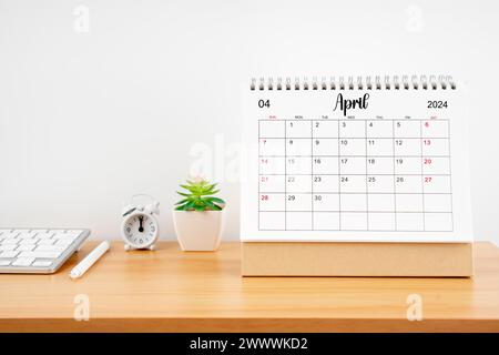 April 2024, monatlicher Schreibtischkalender für 2024 Jahre auf Holztisch mit Wecker. Stockfoto