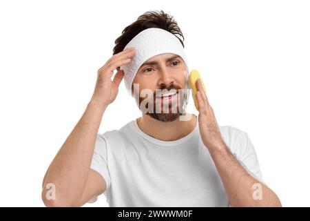 Mann mit Stirnband, der sein Gesicht mit Schwamm auf weißem Hintergrund wäscht Stockfoto