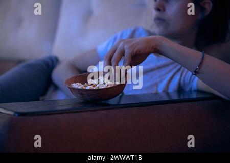 Nahaufnahme einer traurigen Frau, die auf dem Sofa lag und Fernsehen sah und nachts Popcorn aß. Schlaflosigkeit, sucht, Depression, Probleme. Hintergrund mit Kopierraum. Stockfoto