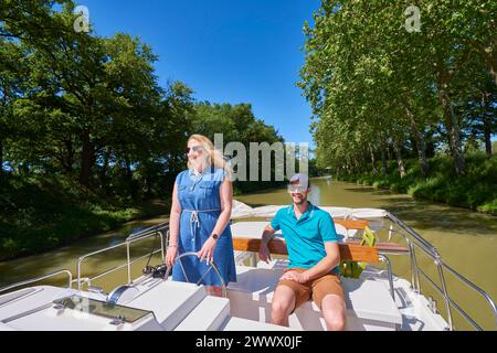 Binnenschifffahrt auf dem Canal du Midi. Frau, die das Boot steuert, navigiert auf dem Kanal der Canal du Midi ist als UNESCO-Weltkulturerbe eingetragen. Stockfoto