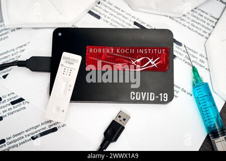 Augsburg, Bayern, Deutschland - 26. März 2024: Symbolisches Bild der RKI-Protokolle zu COVID-19. Auf geschwärzten Dokumenten liegt eine Festplatte mit dem Logo des RKI Robert Koch Institute zusammen mit FFP2-Masken, Spritze und Schnelltest. PHOTOMONTAGE *** Symbolbild RKI-Protokolle zu COVID-19. Eine Festplatte mit dem RKI Robert-Koch-Institut Logo liegt auf geschwärzten Dokumenten zusammen mit FFP2-Masken, Spritze und Schnelltest. FOTOMONTAGE Stockfoto