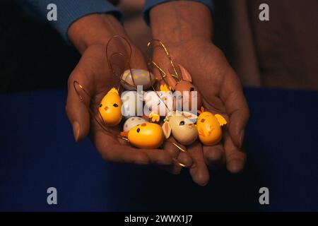 Frau, die Osterspielzeug-Anhänger in der Hand hält. Festliches Weihnachtsspielzeug mit Ostermotiv. Frühlingshasen-Küken. Eiförmige Dekorationen. Farbenfrohe trin Stockfoto
