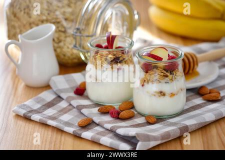Knuspriges Müsli mit Joghurt, Apfel, Nüssen und Banane in Glasgläsern auf Holztisch. Gesundes Frühstückskonzept. Stockfoto