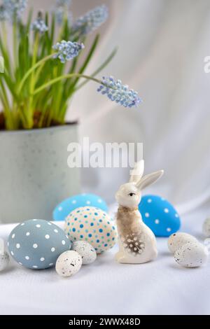 Osterkomposition mit weißem Kaninchen, Eiern und Frühlingsblumen. Osterstillleben Stockfoto