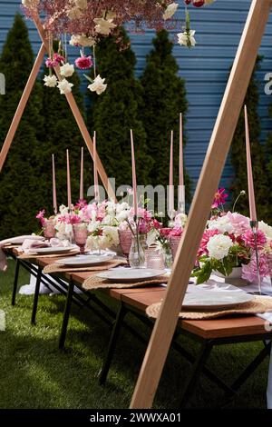 Eleganter Tisch im Freien mit hohen rosafarbenen Kerzen. Romantisches kulinarisches Erlebnis, Sommer-Picknick im Garten Stockfoto