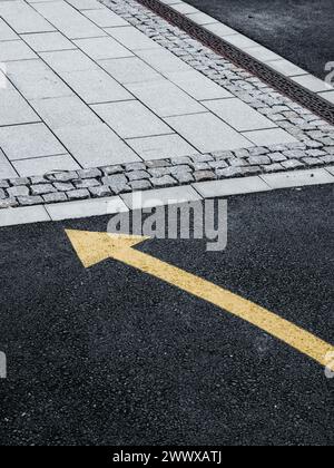 Ein frisch bemalter gelber Pfeil zeigt direkt auf den dunklen Asphalt einer schwedischen Straße, der die Richtung des Verkehrsflusses anzeigt oder Fußgänger führt. Stockfoto