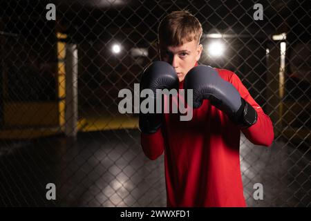 Porträt eines jungen, selbstbewussten männlichen Boxers, der in Pose steht und bereit ist, im Fitnessstudio zu kämpfen Stockfoto