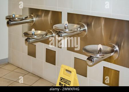 Abbildung mit einem Warnschild in einem Bereich mit Trinkbrunnen, das die Bedeutung der Sicherheit in öffentlichen Räumen unterstreicht. Stockfoto