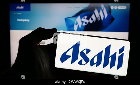 Person, die ein Mobiltelefon mit dem Logo des japanischen Brauunternehmens Asahi Group Holdings Ltd. Vor der Webseite von Business hält. Schwerpunkt auf dem Display des Telefons. Stockfoto