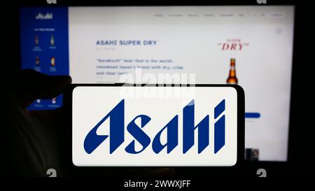 Person, die ein Mobiltelefon mit dem Logo des japanischen Brauunternehmens Asahi Group Holdings Ltd. Vor der Webseite hält. Schwerpunkt auf dem Display des Telefons. Stockfoto