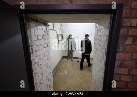 26. März 2024, Sachsen, Kšnigstein: Ein Teilnehmer der Pressetour der neuen Ausstellung „Kernbunker und Pulvermagazin“ geht in einem ehemaligen Bunker für den DDR-Zivilschutz auf der Festung Königstein an einer Schaufensterpuppe mit Schutzanzug und Gasmaske vorbei. Die Festung Königstein macht Räume des einst geheimen DDR-Bunkers im Festungswald, die in der Ausstellung selten zu sehen sind, im Rahmen von Führungen zugänglich. Foto: Robert Michael/dpa Stockfoto