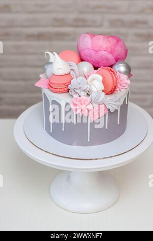 Schöner und eleganter grauer Kuchen, dekoriert mit geschmolzener weißer Schokolade, Makronen, rosa Pfingstrosenblüten und Baisons. Idee für Hochzeit oder Geburtstag Stockfoto