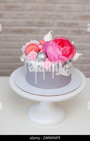 Schöner und eleganter grauer Kuchen, dekoriert mit geschmolzener weißer Schokolade, Makronen, rosa Pfingstrosenblüten und Baisons. Idee für Hochzeit oder Geburtstag Stockfoto