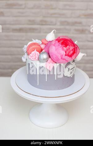 Schöner und eleganter grauer Kuchen, dekoriert mit geschmolzener weißer Schokolade, Makronen, rosa Pfingstrosenblüten und Baisons. Idee für Hochzeit oder Geburtstag Stockfoto