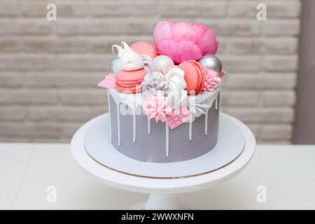Schöner und eleganter grauer Kuchen, dekoriert mit geschmolzener weißer Schokolade, Makronen, rosa Pfingstrosenblüten und Baisons. Idee für Hochzeit oder Geburtstag Stockfoto