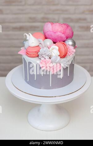 Schöner und eleganter grauer Kuchen, dekoriert mit geschmolzener weißer Schokolade, Makronen, rosa Pfingstrosenblüten und Baisons. Idee für Hochzeit oder Geburtstag Stockfoto